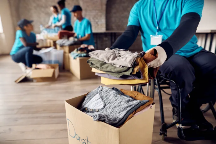 Close-up of man in wheelchair packing clothing in donation box while volunteering at community center.